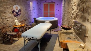 A spa room with a massage table, a hot tub, a statue, and a wooden table with a bowl of fruit. - Chambres d'hôtes Peu del Causse SPA (Sainte-Colombe-de-la-Commanderie)
