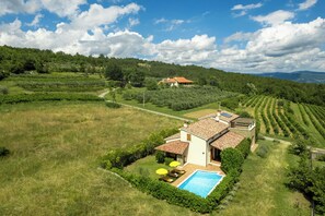 A house with a swimming pool, surrounded by green fields and a hilly landscape.