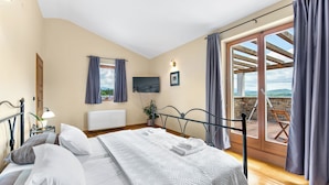 Een slaapkamer met een bed, een televisie, een raam met gordijnen, een plant en uitzicht op het landschap.