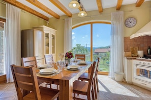 Un coin repas avec une table en bois dressée pour quatre personnes, une cuisine équipée d’une cuisinière et une grande fenêtre donnant sur l’extérieur.