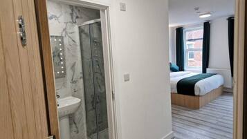 A modern bedroom with a bed, a shower area, and a view of a brick building.