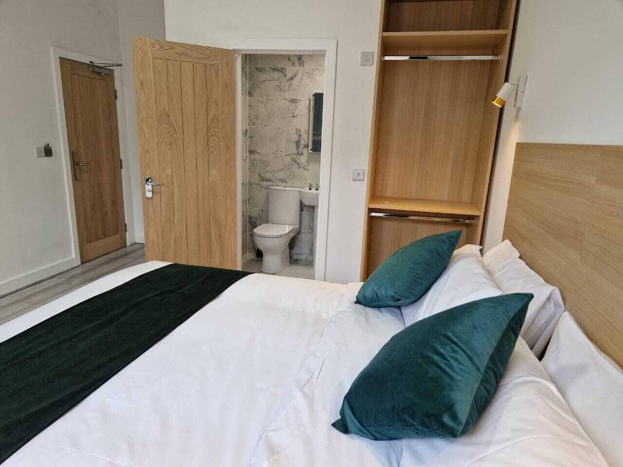 A bedroom with a bed, two pillows, a wooden wardrobe, and a bathroom visible through an open door.