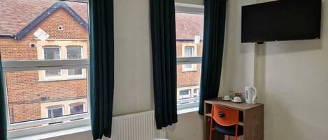 A hotel room with a bed, a desk with a chair, a TV mounted on the wall, and a window with curtains.