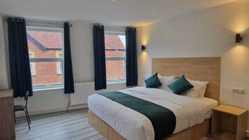A modern bedroom with a large bed, a wooden headboard, a bedside table, and a view of a brick building through the window.