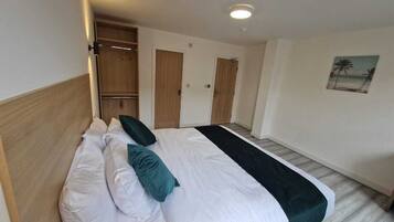 A hotel room with a bed, a wooden headboard, a black throw blanket, and a painting of a beach scene.