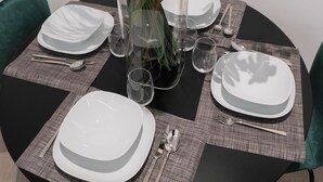 A round dining table set with white plates, silverware, and clear glasses, surrounded by green chairs. - 2 Bedroom Apartment in Taranto (Taranto)