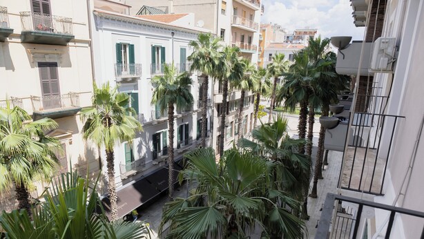 A narrow street lined with palm trees and multi-story buildings with balconies. - 2 Bedroom Apartment in Taranto (Taranto)