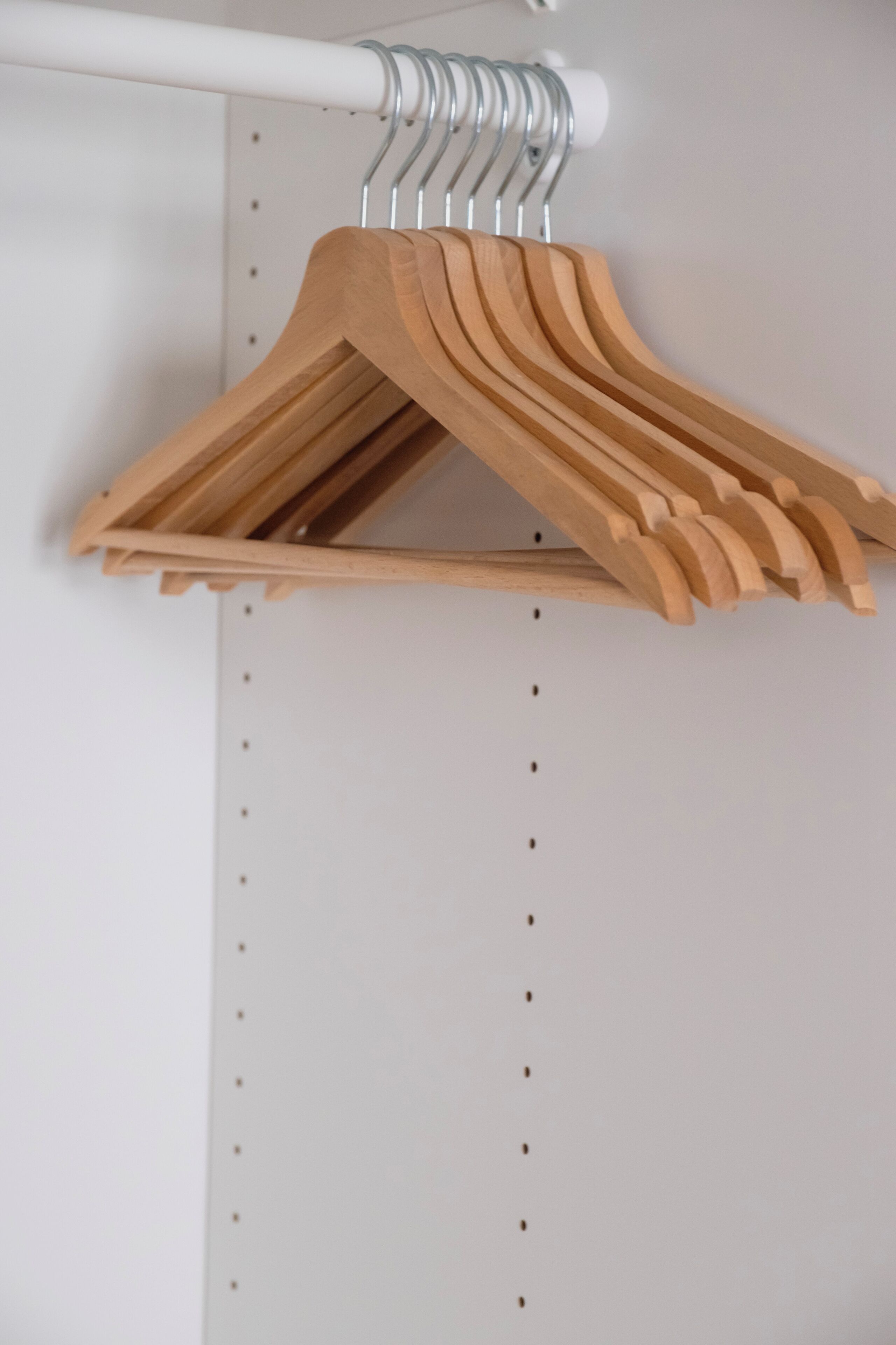 A wooden hanger rack with multiple hangers against a white wall.
