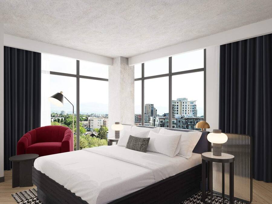 A modern bedroom with a large bed, a red chair, and a city view through large windows.