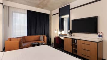 A hotel room with a large bed, a sofa, a desk with a mirror, and a TV.