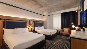 A hotel room with two beds, a desk, a chair, a TV, and a window with curtains.