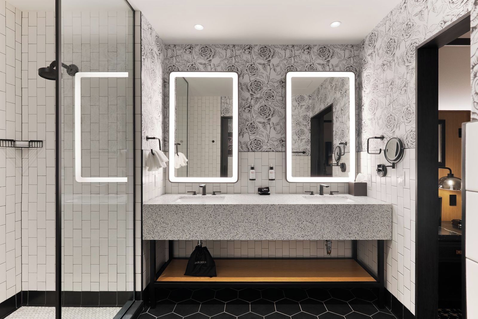 A modern bathroom with two mirrors, a shower, and a vanity with a speckled countertop.