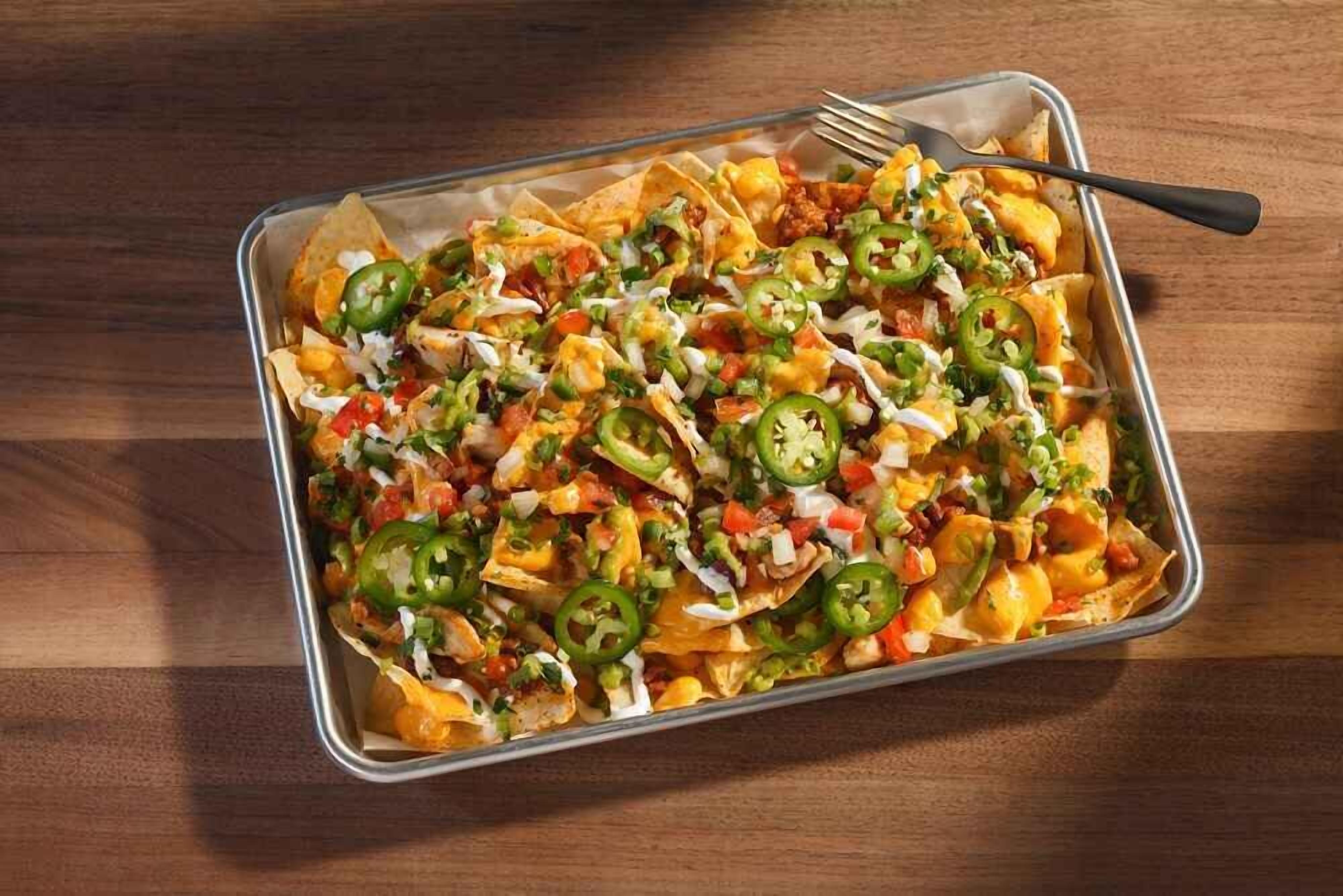 Nachos belegd met kaas, jalapeños en een romige saus in een metalen bak.