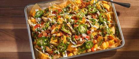Nachos belegd met kaas, jalapeños en een romige saus in een metalen bak.