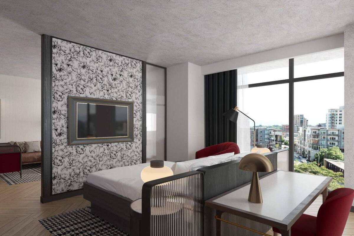 Ein modernes Hotelzimmer mit einem großen Bett, einem Schreibtisch mit Stuhl, einem Fernseher und Blick auf die Stadt durch große Fenster.