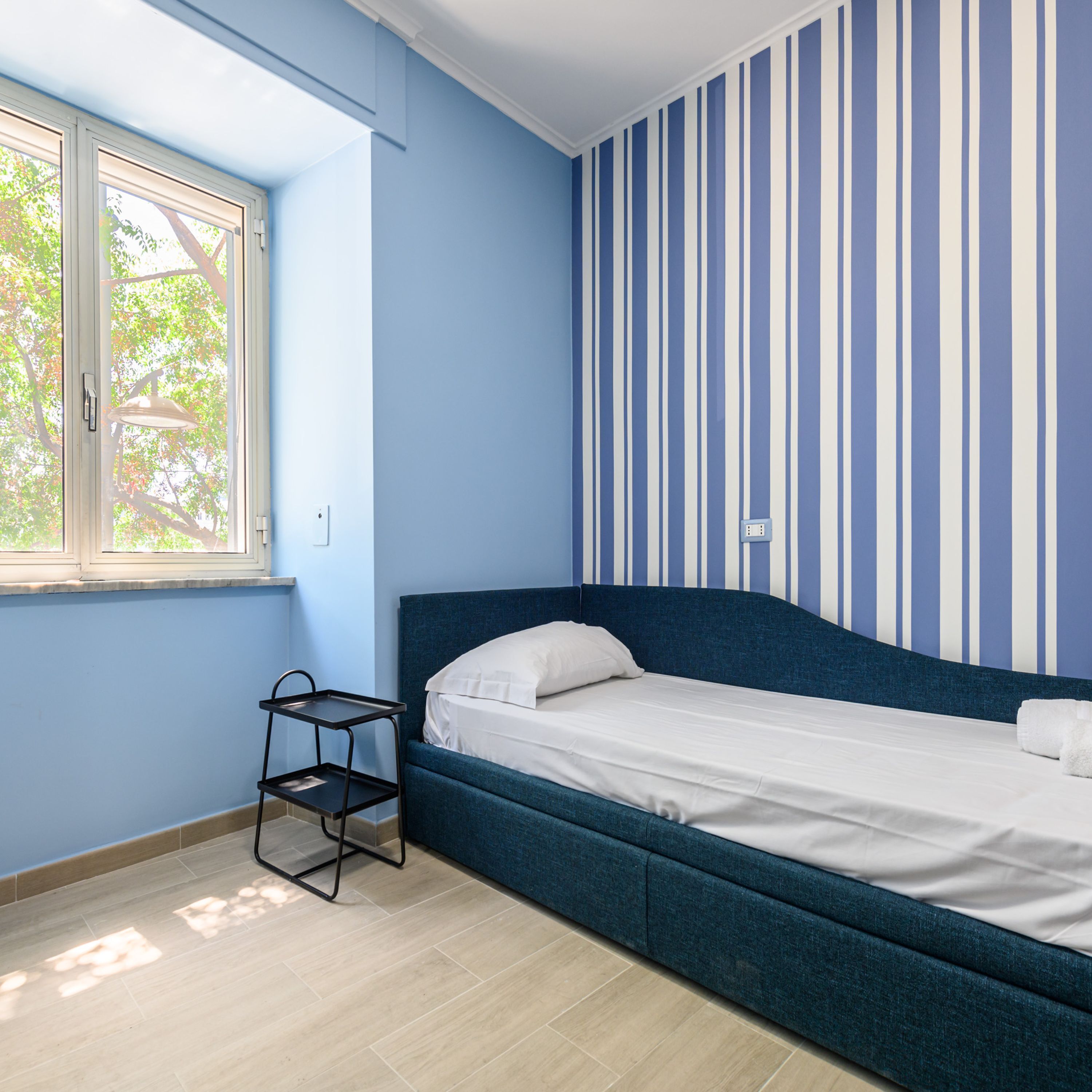 A bedroom with a single bed, a window, and a striped wall.