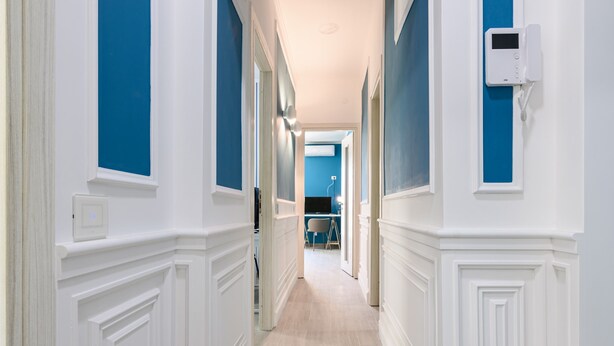 A hallway with white wainscoting and blue walls, leading to a room with a blue accent wall. - Via Nuova Marina 121 - Appartamento 1 (Naples)