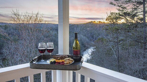 Un balcon avec un plateau sur lequel se trouvent deux verres de vin rouge, une bouteille de vin et une assiette de collations.