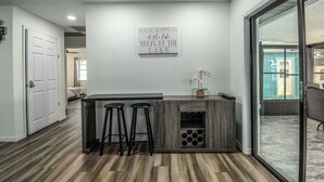 Una cocina moderna con una isla central, dos taburetes de bar, un letrero decorativo y vistas al exterior.