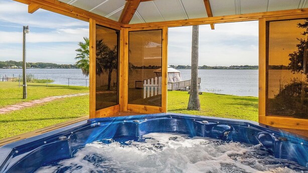 Un jacuzzi con techo de madera y paredes de vidrio, con vistas a un lago y una zona verde.