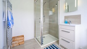 Une salle de bain moderne avec une douche à parois de verre, un meuble-lavabo blanc avec un miroir et une caisse en bois posée sur le sol.