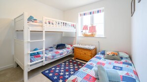 Une chambre d’enfant avec des lits superposés, une fenêtre avec des rideaux à rayures et un tapis orné de motifs en forme d’étoiles.