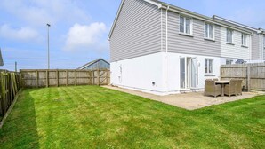 Une maison à deux étages avec un jardin clôturé, une terrasse dotée de mobilier d’extérieur et un ciel dégagé.
