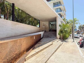 A modern building with a staircase leading to an entrance, a concrete bench, and a clear sky.