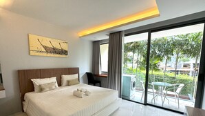 A modern hotel room with a large bed, a desk, and a balcony with a view of greenery.