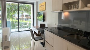 A modern kitchen with a large island, a dining area with chairs, and a view of greenery outside.