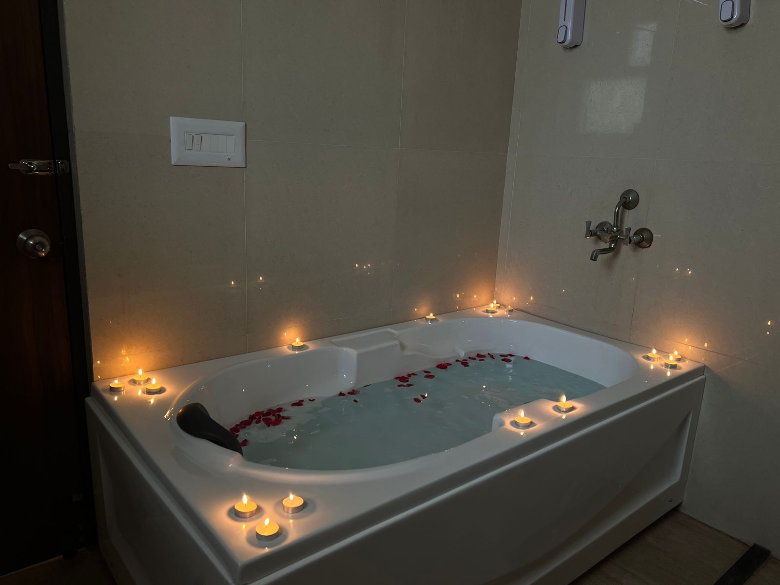 Eine Badewanne mit Kerzen und Rosenblättern, eine Duschbrause und eine Tür.