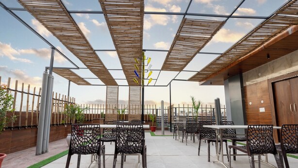 An outdoor patio with tables and chairs, a wooden fence, and a view of the sky. - Letstay Business Suite (Noida)