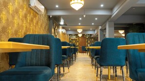 A hotel lobby with rows of teal chairs, wooden tables, and a chandelier. - Letstay Business Suite (Noida)