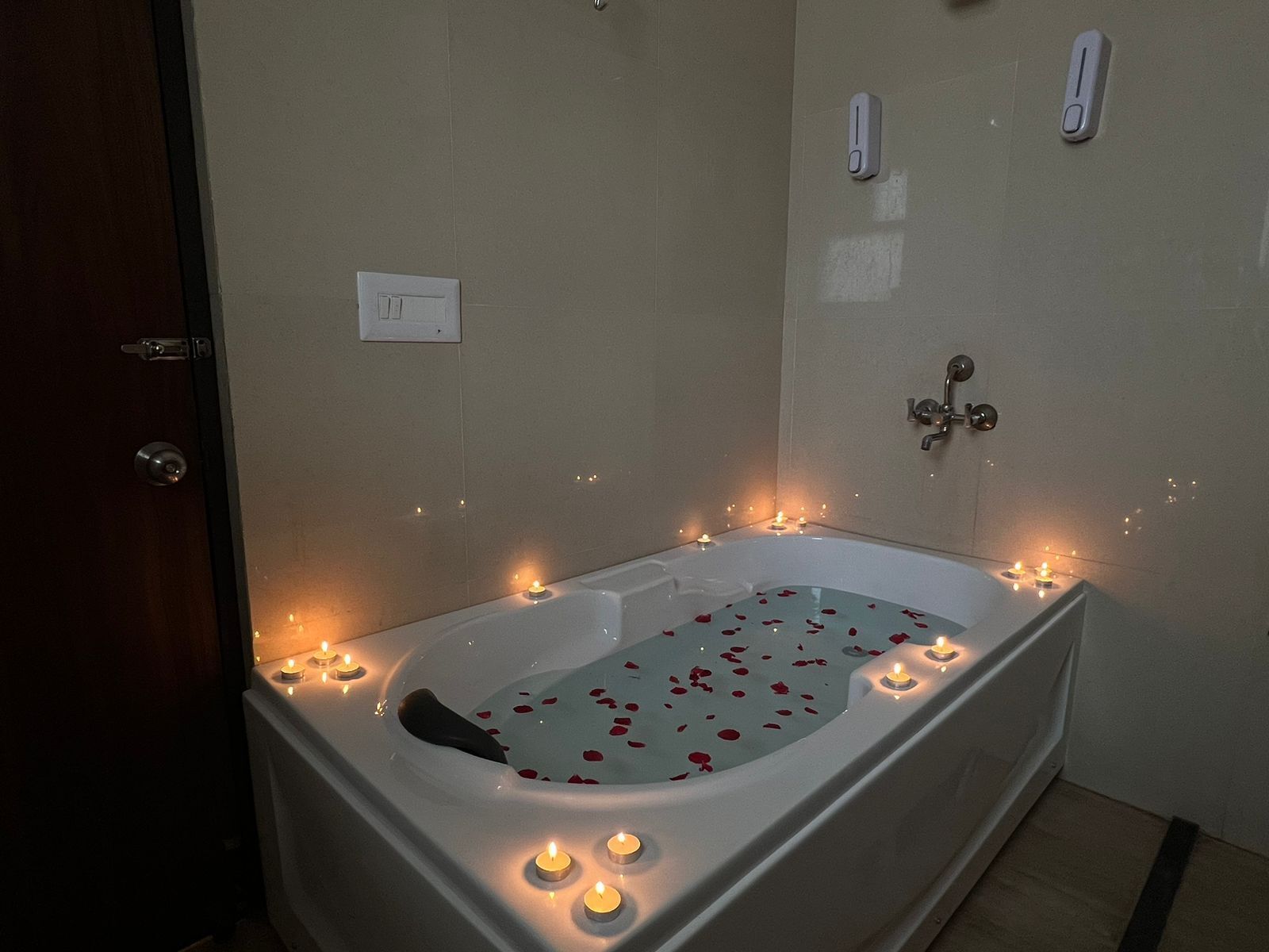 A bathtub with rose petals and candles, indicating a romantic setting.
