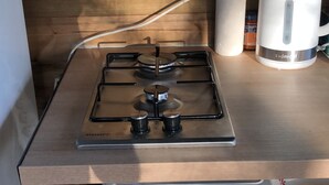 A compact kitchen with a gas stove, a microwave, and a kettle on a wooden countertop.