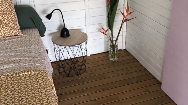 A room with a bed, a small round table with a lamp, and a plant in a vase.