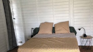 A bedroom with a wooden bed, patterned bedding, a small bedside table with a lamp, and a window with curtains.