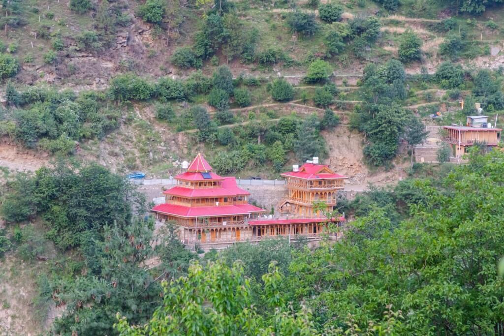 A traditional multi-tiered building with a red roof, surrounded by lush greenery and terraced fields.