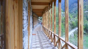 A corridor with wooden beams and stone walls, leading to a scenic outdoor view. - Tirthan Village Resort (Banjar)