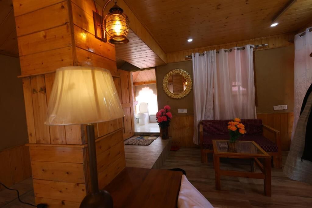 Et interiør af en træhytte med en sofa, et bord med blomster, en lampe og et spejl på væggen.