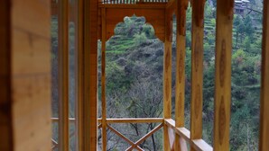 A wooden balcony with a view of a forested hillside. - Tirthan Village Resort (Banjar)