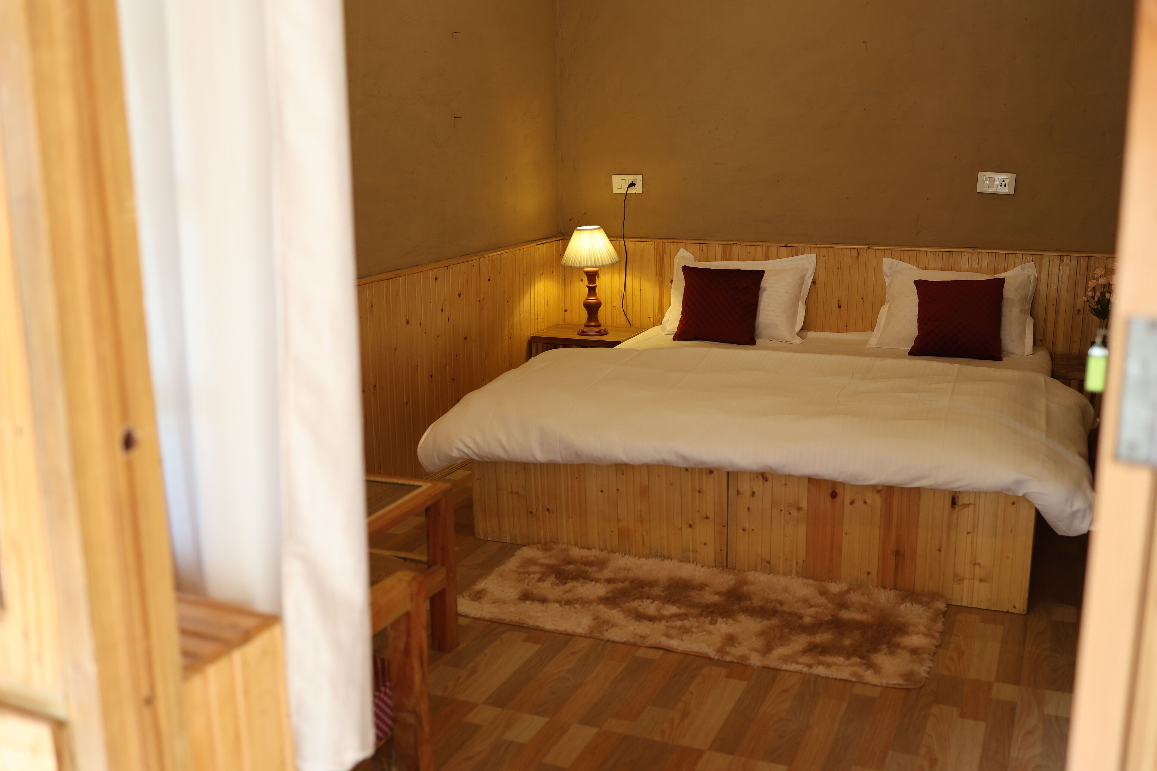 A wooden-framed bedroom with a bed, a nightstand, a lamp, and a rug.