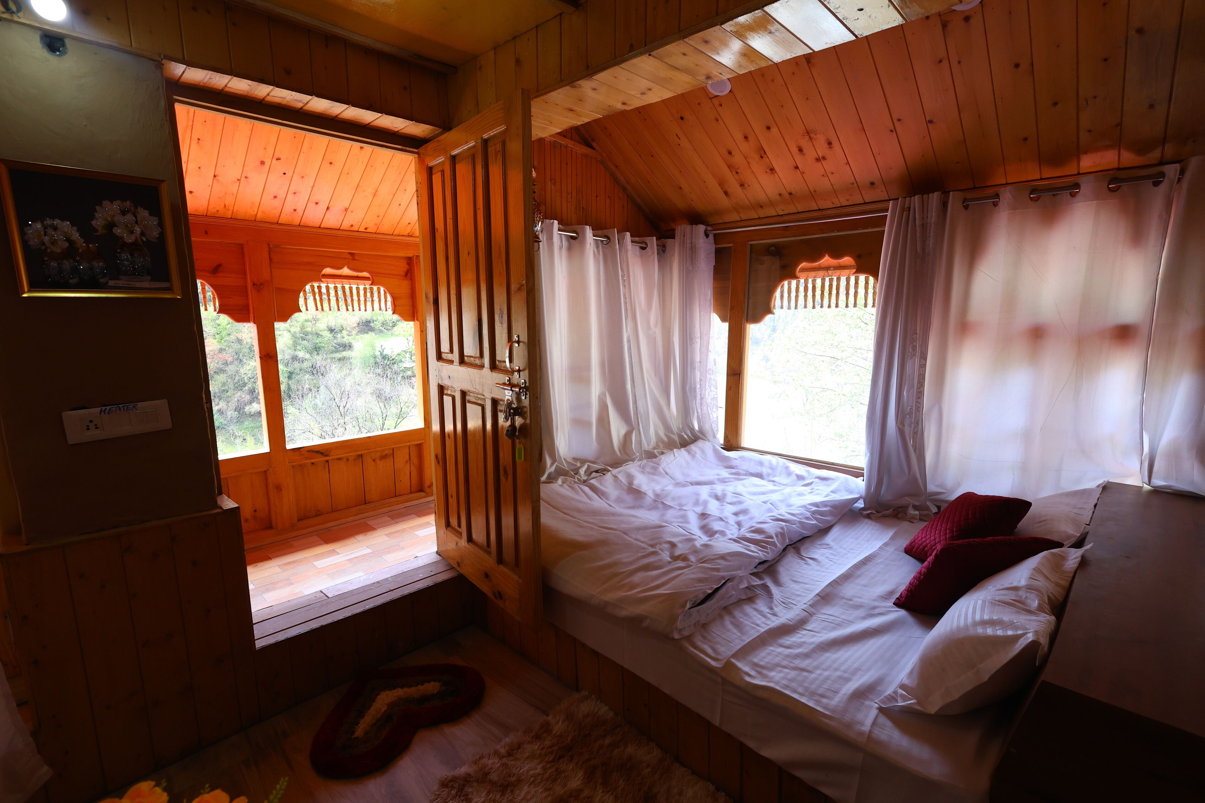 Een slaapkamer in een houten hutje, met een bed, een bankje en een raam met gordijnen.