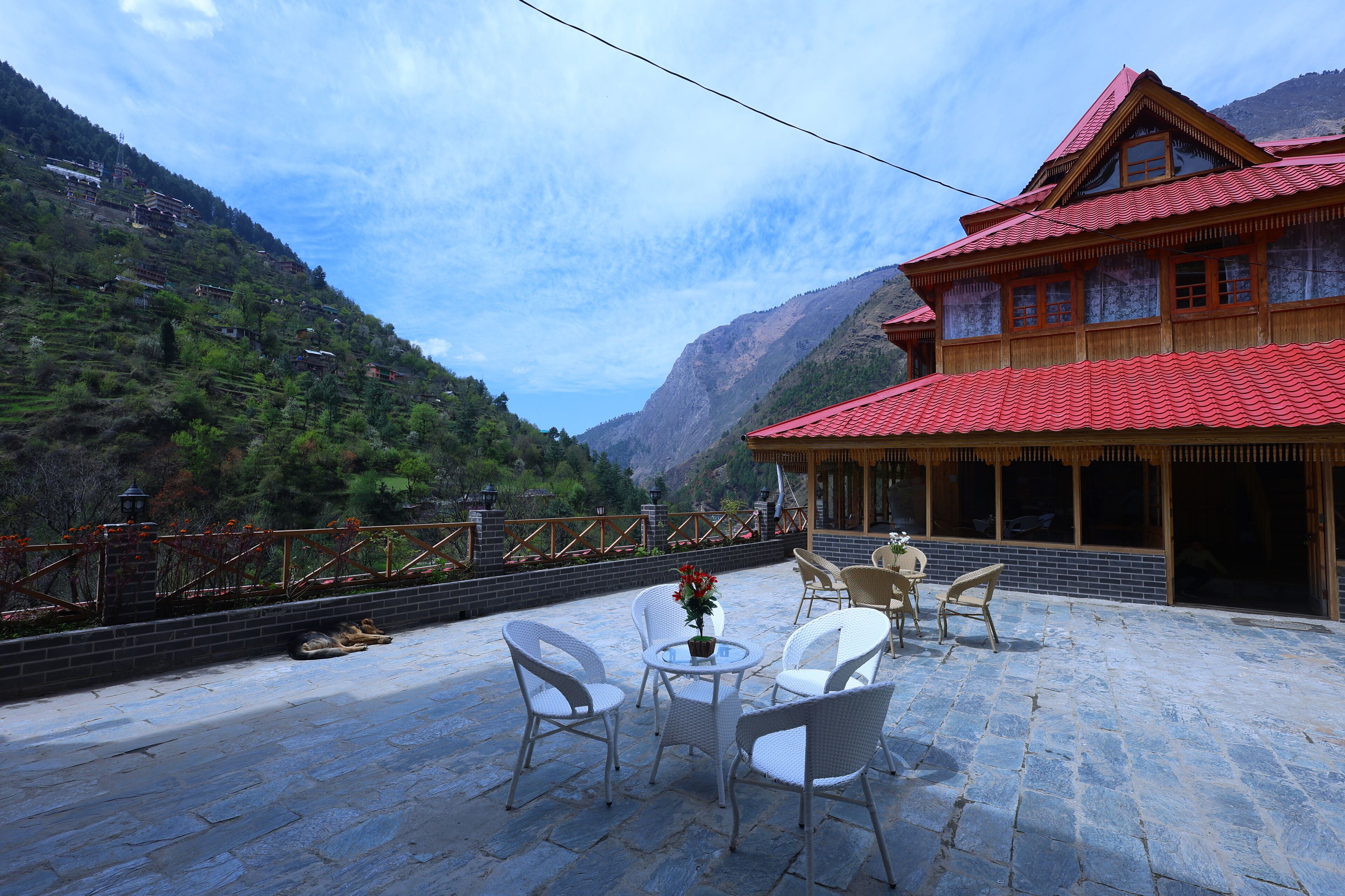 A traditional wooden building with a red roof and a balcony with white wicker chairs and a table.
