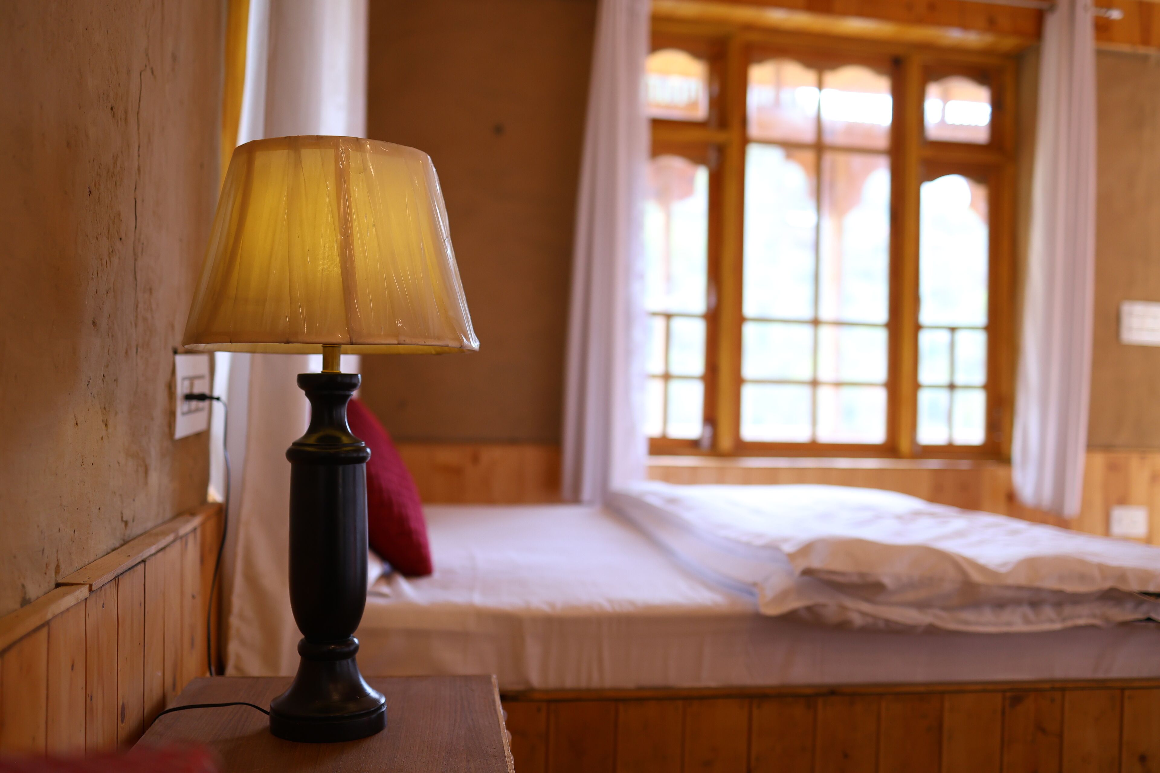 A wooden room with a bed, a lamp, and a window with curtains.