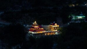 A traditional multi-tiered building with a central spire, surrounded by a well-lit perimeter. - Tirthan Village Resort (Banjar)