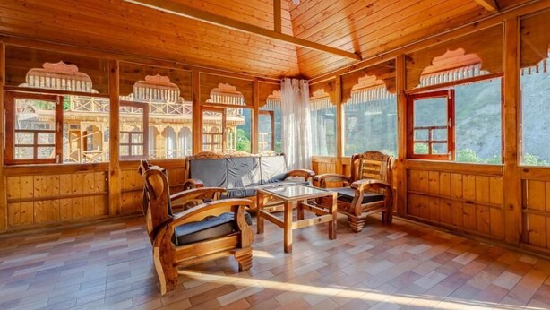 A wooden cabin interior with a sofa set, wooden chairs, and a coffee table. - Tirthan Village Resort (Banjar)