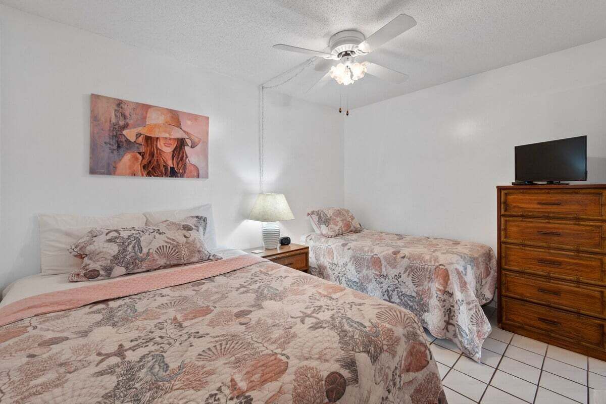 A bedroom with two beds, a ceiling fan, a TV, and a wooden dresser.