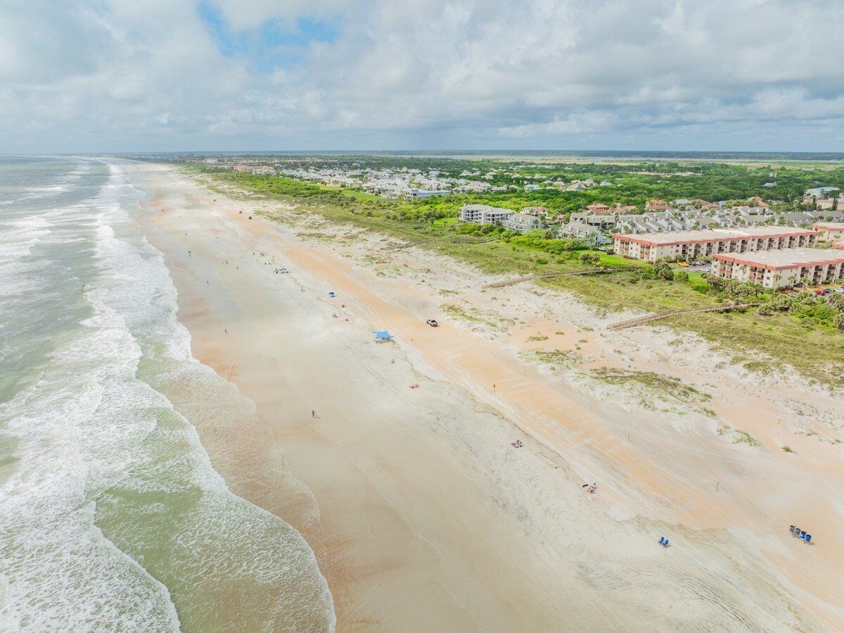 A coastal area with a beach, a large building complex, and a distant view of the ocean.