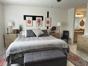 Un dormitorio con cama, mesitas de noche, una silla, cómoda y cuadros en la pared.